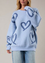 Load image into Gallery viewer, Light blue sweater with heart patterns worn by a person on a neutral background