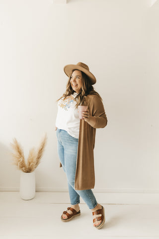 Plus size woman wearing jeans, a graphic tee, long cardigan and boho hat.