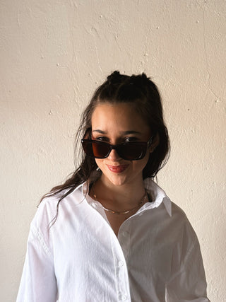 Woman wearing a white shirt and sunglasses against a plain wall
