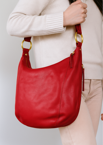 Red handbag with gold handle held by a person wearing a beige sweater and pants on a light gray background