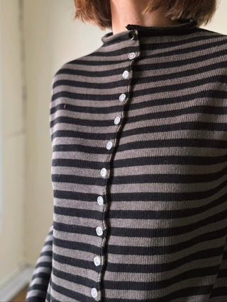 A woman wearing a black and gray horizontally striped knit top with a buttoned front, photographed indoors near a window.