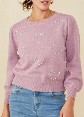 Person wearing a pink sweater with heart patterns on a beige background