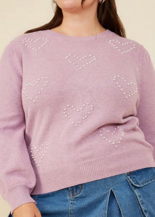 Person wearing a light purple sweater with heart patterns and blue jeans on a beige background