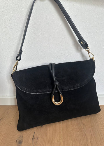 Black handbag with a gold clasp on a wooden floor against a white wall