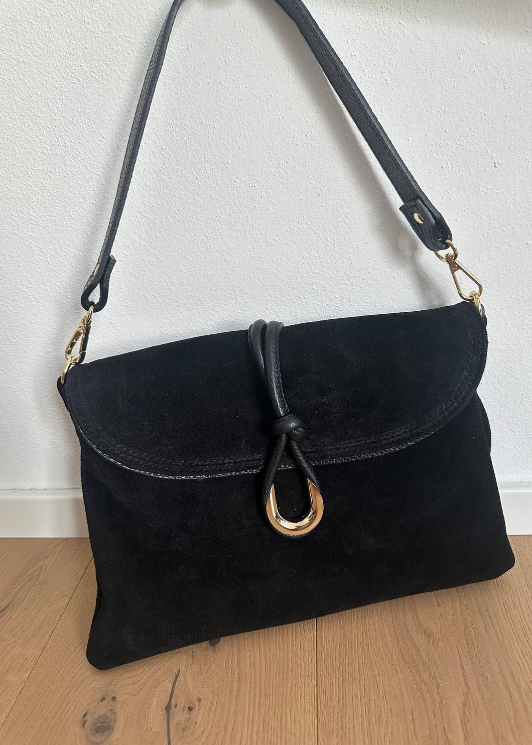 Black handbag with a gold clasp on a wooden floor against a white wall
