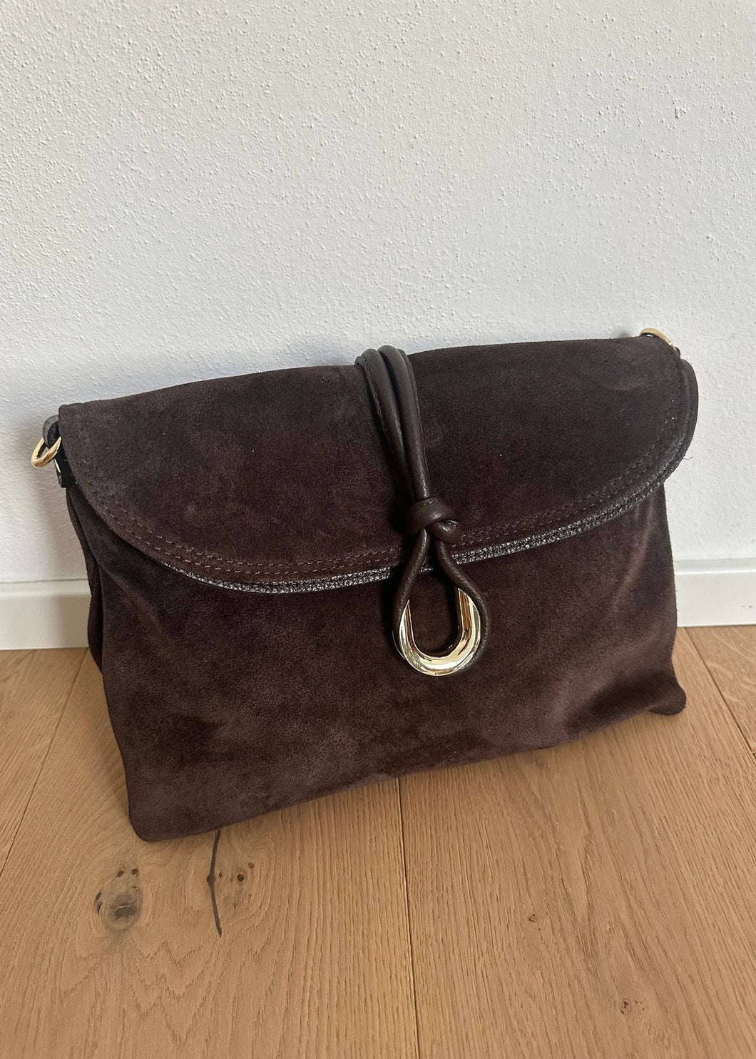 Brown suede handbag with a gold clasp on a wooden floor.