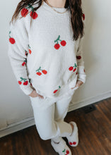 Load image into Gallery viewer, Person wearing a white sweater with red cherry designs in a home setting.
