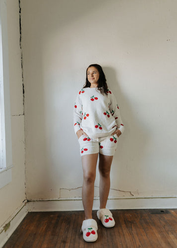 Person wearing a white outfit with red cherry patterns in a room with wooden floor and white walls.