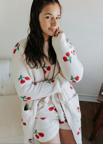 Woman wearing a white robe with red cherry patterns in a casual setting.