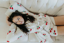 Load image into Gallery viewer, Woman wearing a white robe with red cherry patterns, lying on a beige couch.
