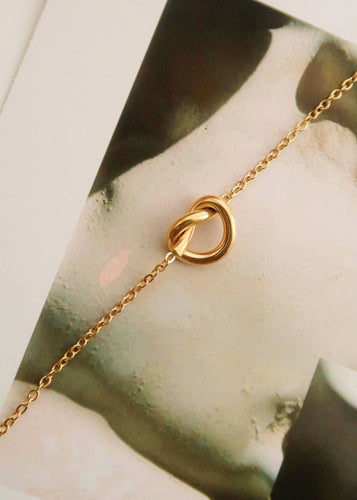 Gold necklace with a unique clasp design on a marble surface