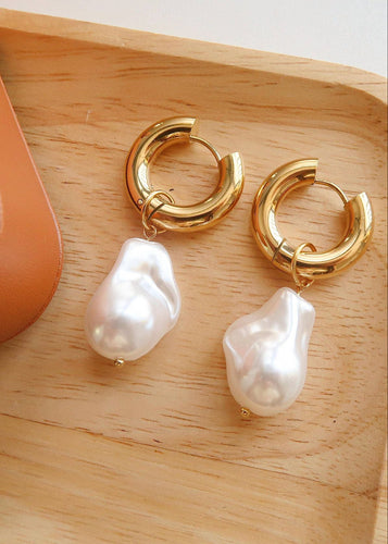 Gold hoop earrings with pearl drops on a wooden surface