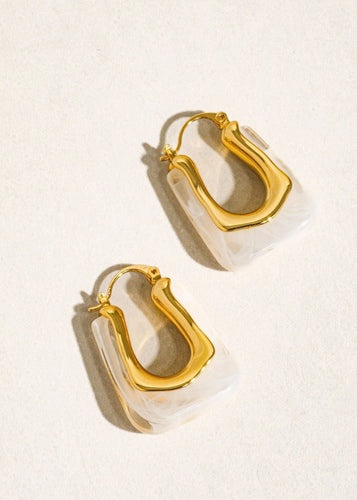 Gold hoop earrings with clear acrylic accents on a light beige background