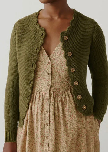 Green knitted cardigan over a floral dress on a neutral background