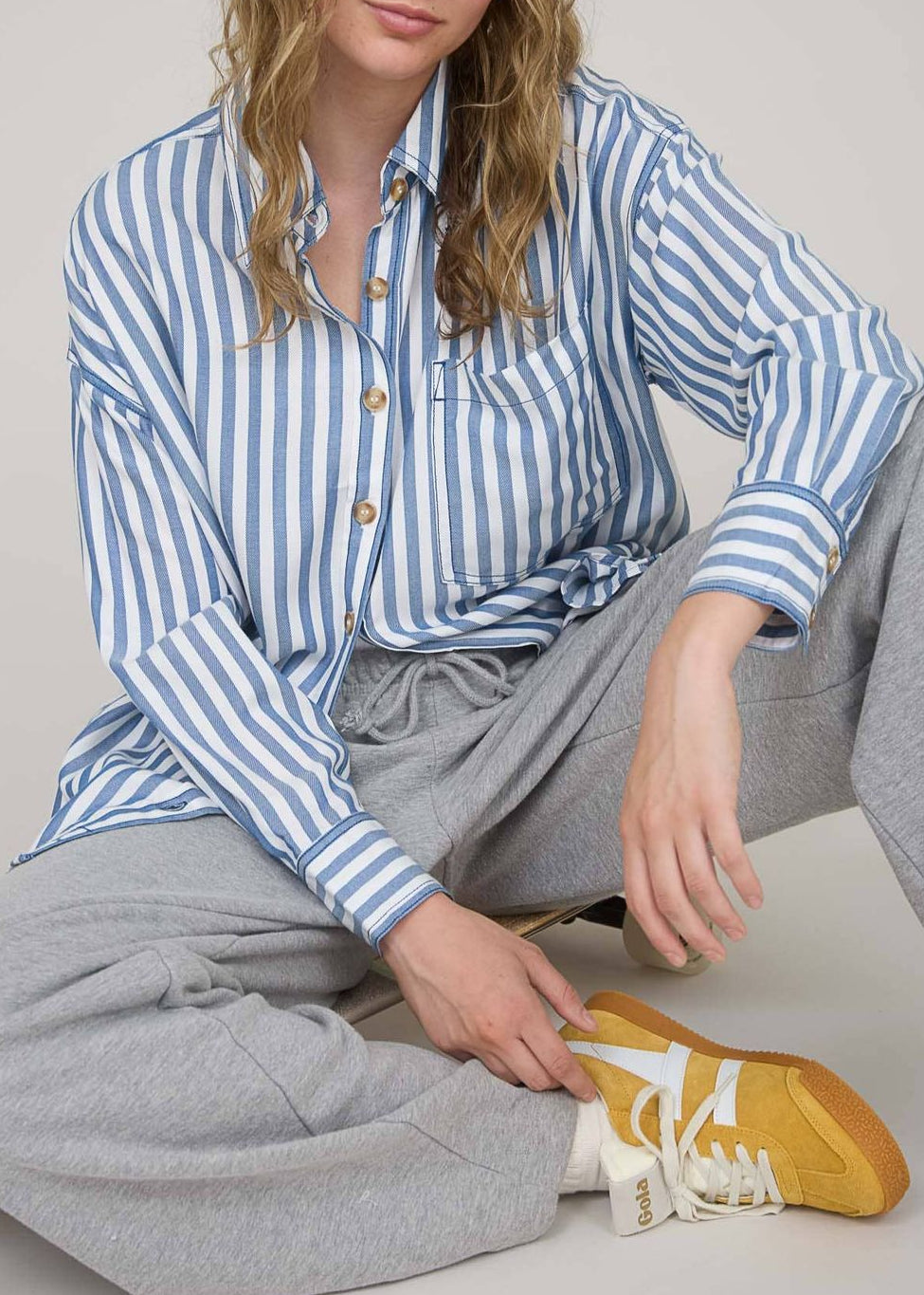 Woman wearing a blue and white striped shirt and gray pants, sitting on the floor with a yellow shoe.