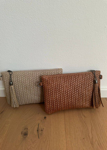 Two woven clutch bags, one beige and one brown, on a wooden surface with a light background.