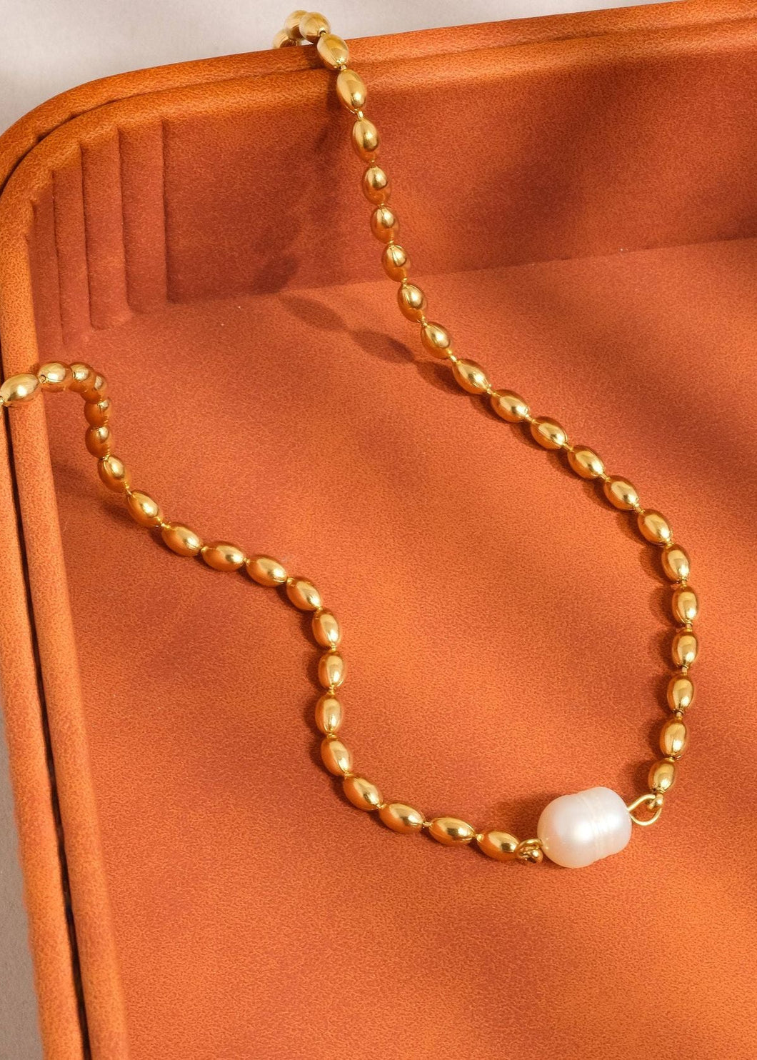 Gold necklace with a pearl pendant on an orange surface