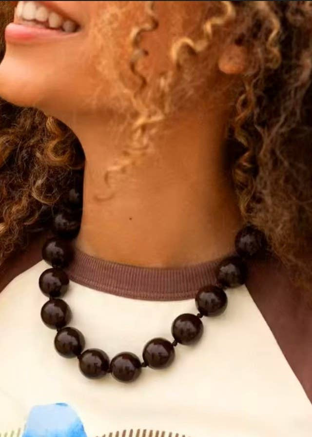 Woman wearing a dark brown beaded necklace with a blurred background