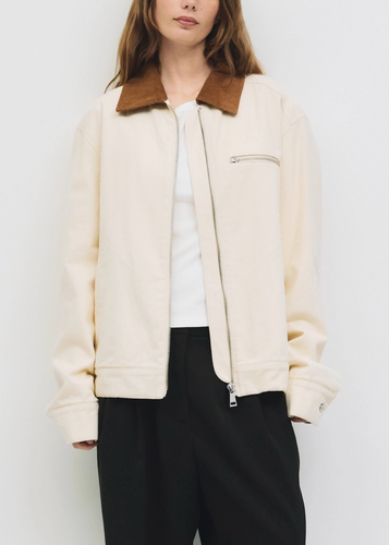 Person wearing a cream jacket and black pants against a white background