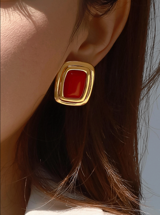 Close-up of a gold earring with a red stone worn by a person.