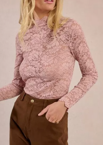 Woman wearing a pink floral blouse and brown pants against a beige background