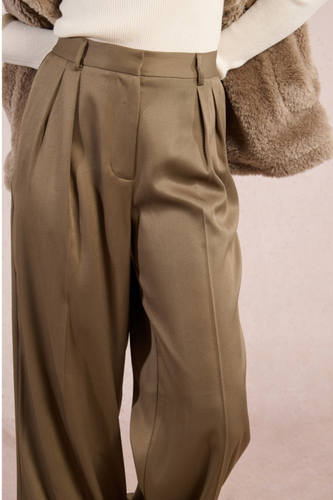 Brown pleated pants worn with a textured brown coat on a light pink background