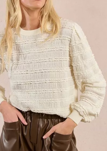 Person wearing a textured white sweater and brown leather shorts on a beige background