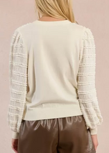 Load image into Gallery viewer, Person wearing a cream sweater with textured sleeves and brown shorts on a beige background
