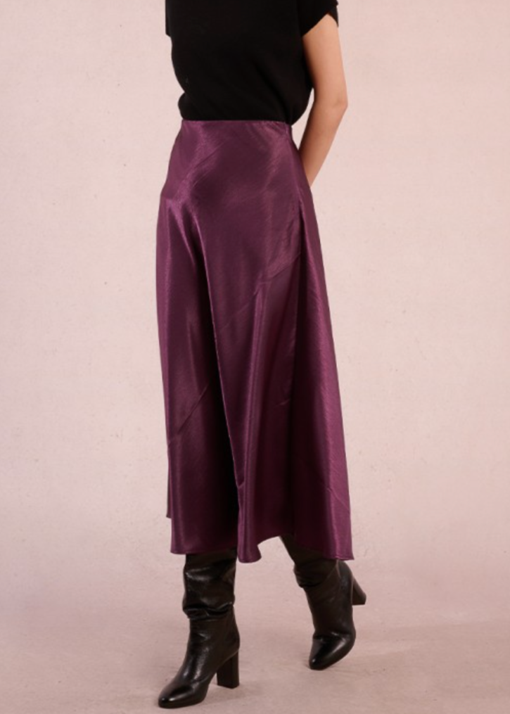 Person wearing a long purple skirt and black boots on a plain background