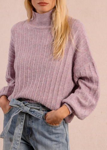 Person wearing a pink sweater and blue jeans against a beige background