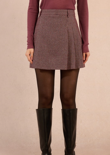 Person wearing a patterned skirt, maroon sweater, brown tights, and black knee-high boots on a beige background