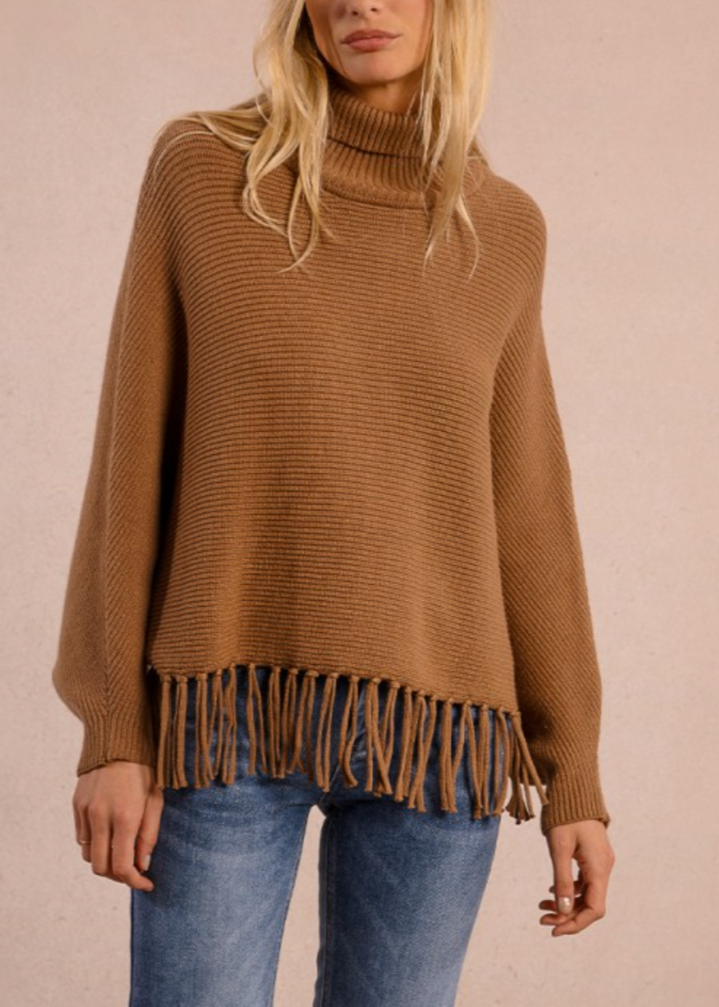 Woman wearing a brown fringed sweater against a plain background