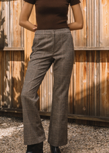 Load image into Gallery viewer, Person wearing brown checkered pants and a black top against a wooden wall.
