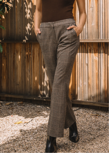 Person wearing checkered flared pants and a brown top against a wooden fence.