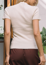 Load image into Gallery viewer, Woman wearing a white top and brown pants with plants in the background
