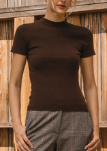 Load image into Gallery viewer, Woman wearing a brown short-sleeve top and plaid pants against a wooden fence.
