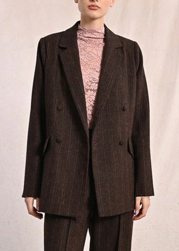 Woman wearing a brown suit with a pink turtleneck against a plain background