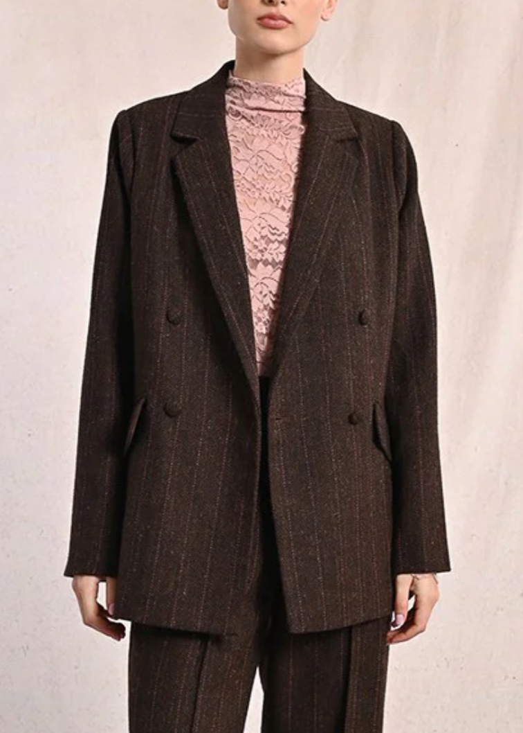 Woman wearing a brown suit with a pink turtleneck against a plain background