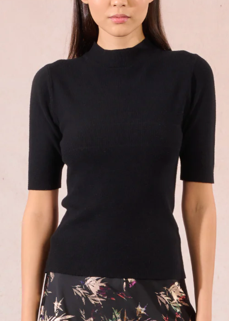 Person wearing a black top and floral skirt against a beige background
