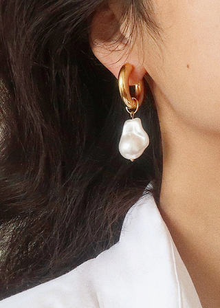 Close-up of a person wearing a gold hoop earring with a pearl pendant.