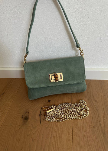 Green handbag with gold chain on a wooden floor against a white wall